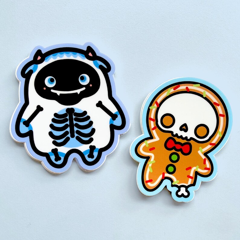 Pu&ograve; includere: Due adesivi fustellati con personaggi a tema Halloween. Uno &egrave; un mostro bianco con volto nero e dettagli blu, l'altro &egrave; uno scheletro di omino di pan di zenzero con glassa arancione e papillon rosso.