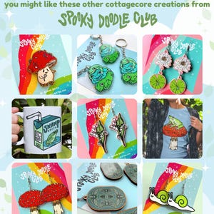 May include: A collection of cottagecore-themed earrings, keychains, and a mug featuring mushrooms, frogs, flowers, and snails. The items are all decorated with a rainbow and the text "Spooky Doodle Club".