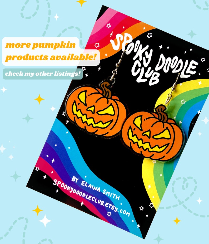 May include: A pair of pumpkin-shaped earrings with a spooky doodle club logo on the card. The earrings are orange with a yellow face and black eyes. The card is rainbow colored with white stars.
