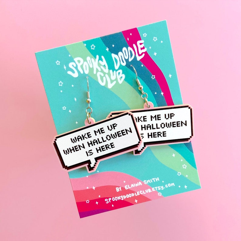 May include: Pink and white pixelated speech bubble earrings with the text "Wake me up when Halloween is here". The earrings are on a card with the text "Spooky Doodle Club" and "By Elaina Smith Spookydoodleclub.etsy.com".