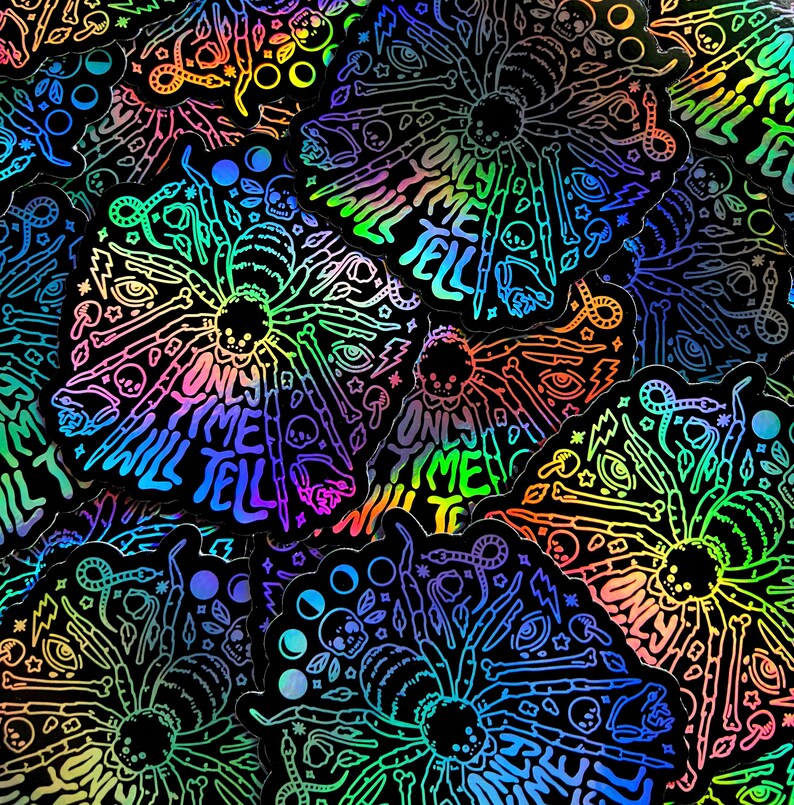 May include: A close-up of several iridescent holographic stickers featuring a spider with the text "Only Time Will Tell". The stickers are black with rainbow holographic foil.