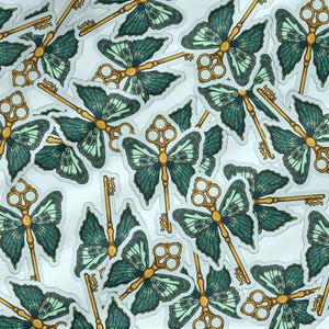 May include: A collection of stickers featuring a gold key with butterfly wings. The wings are a teal and green color with a detailed pattern. The stickers are on a white background.