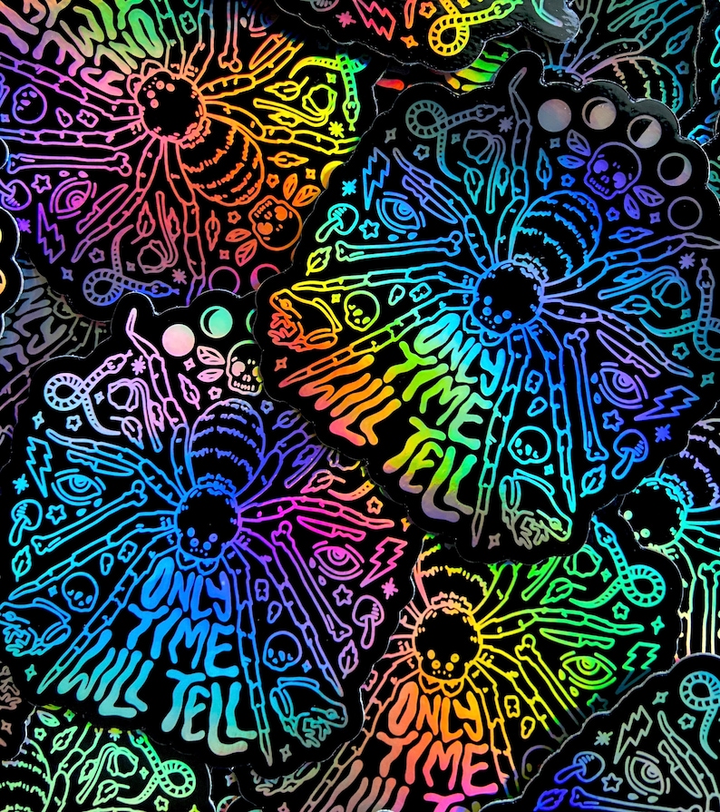 May include: A holographic sticker with a black background and a rainbow iridescent finish. The sticker features a spider with eight legs and the text "Only Time Will Tell". The spider is surrounded by various symbols, including skulls, eyes, mushrooms, and stars.