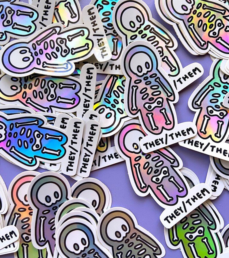 May include: A collection of iridescent holographic stickers featuring a cartoon skeleton figure with the text "They/Them" on each sticker.