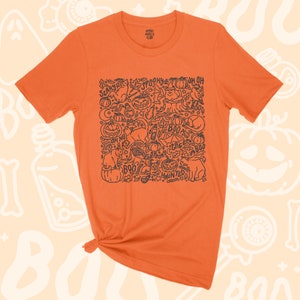 K&ouml;nnte beinhalten: Orangefarbenes T-Shirt mit einer schwarz-wei&szlig;en Illustration einer gruseligen Halloween-Szene. Die Illustration enth&auml;lt K&uuml;rbisse, Katzen, Flederm&auml;use, Geister und die W&ouml;rter "Spooky", "Boo", "Creepy", "Haunted" und "Oh No".