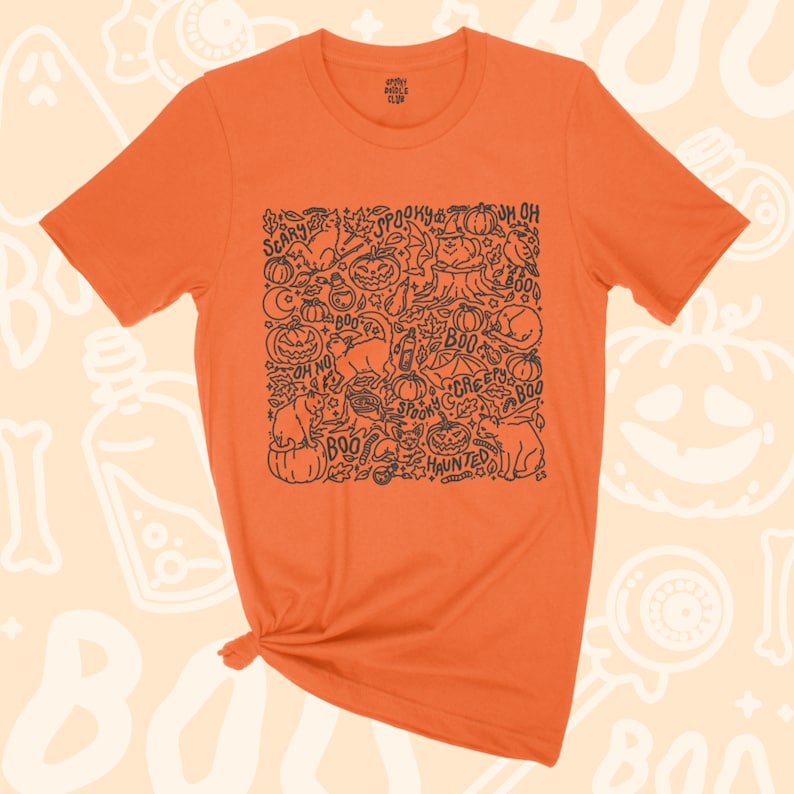 K&ouml;nnte beinhalten: Orangefarbenes T-Shirt mit einer schwarz-wei&szlig;en Illustration einer gruseligen Halloween-Szene. Die Illustration enth&auml;lt K&uuml;rbisse, Katzen, Flederm&auml;use, Geister und die W&ouml;rter "Spooky", "Boo", "Creepy", "Haunted" und "Oh No".