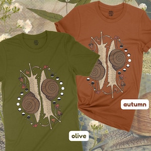 Pu&ograve; includere: Due t-shirt con una grafica di due lumache con funghi e fasi lunari. Le t-shirt sono di colore oliva e autunnale. Il testo "olive" e "autumn" &egrave; stampato sul fondo delle magliette.