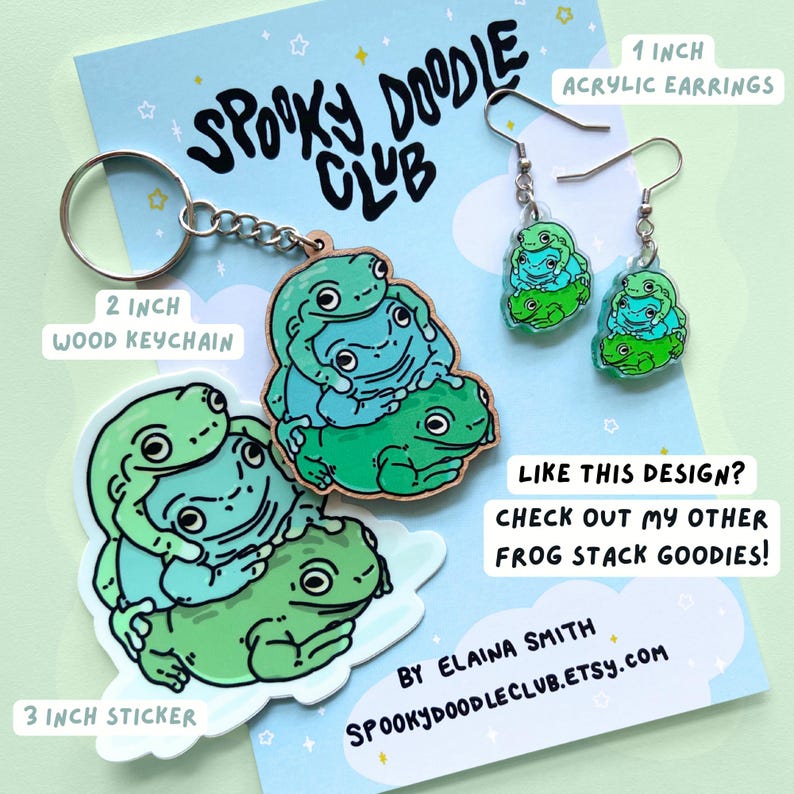 May include: A set of frog stack themed goods, including a 3 inch sticker, a 2 inch wooden keychain, and a pair of 1 inch acrylic earrings. The sticker and keychain feature a stack of three frogs in shades of green and blue. The earrings are also a stack of three frogs, but are smaller and made of clear acrylic. The text "Spooky Doodle Club" is visible in the image.