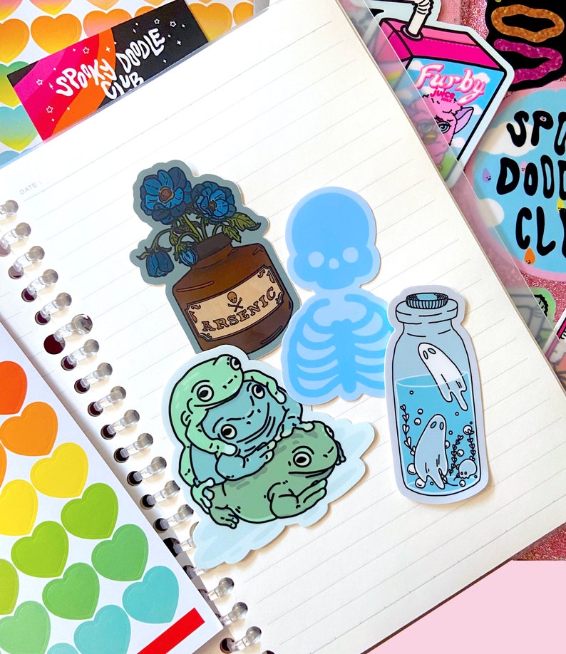 May include: A set of five stickers featuring a blue skeleton, a bottle with a ghost inside, three frogs, and a bottle with blue flowers and the word "ARSENIC" on the label.