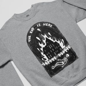 May include: A grey sweatshirt featuring a black and white illustration of a burning house with the text "The End Is Here" above it.