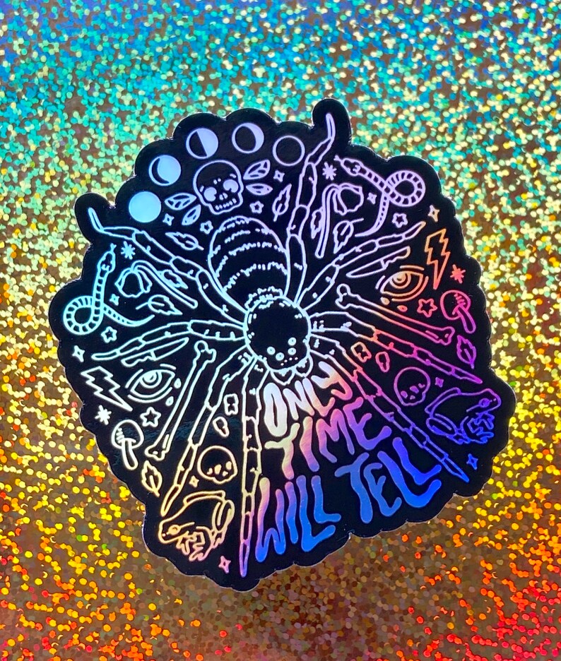 May include: A black and white sticker with a spider design and the text "Only time will tell". The sticker has a holographic finish and features a variety of other designs, including moons, skulls, snakes, and eyes.