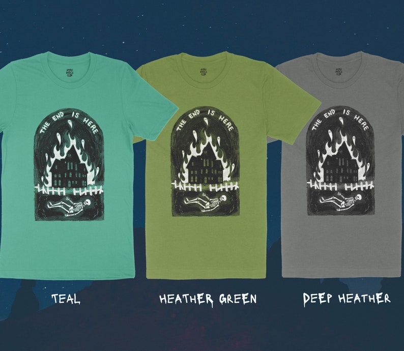 Op de afbeelding: Drie T-shirts met een grafische print van een brandend huis met een skelet dat ervoor ligt. De tekst "THE END IS HERE" is boven het huis gedrukt. De T-shirts zijn teal, heidegroen en diep heidekleurig.