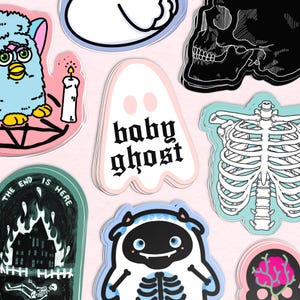 May include: A collection of colorful stickers featuring various designs, including a blue fuzzy creature with a candle, a pink ghost with the text "baby ghost", a skeleton ribcage, a black and white skull, a black and white skeleton in a burning building, and a blue and black creature with a skeleton inside.