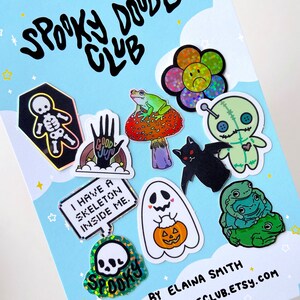 May include: A collection of spooky themed stickers featuring a skeleton, a ghost holding a pumpkin, a frog on a mushroom, a voodoo doll, a bat, a skull, a rainbow hand with the words "Good Juju", and a sign that says "I have a skeleton inside me".