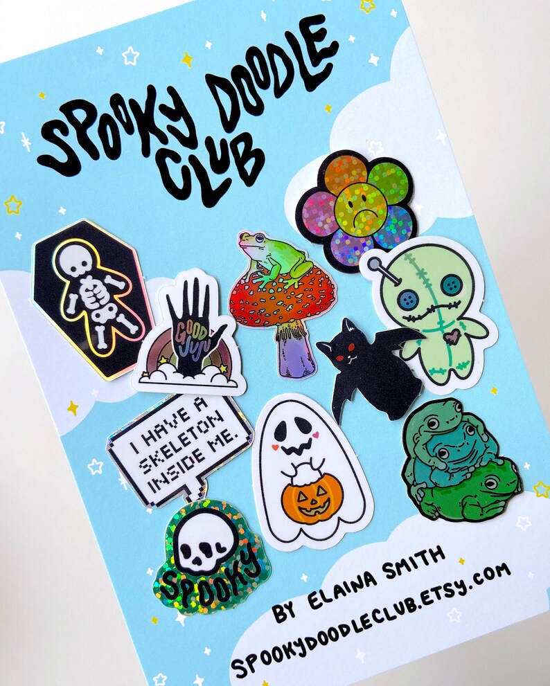 May include: A collection of spooky themed stickers featuring a skeleton, a ghost holding a pumpkin, a frog on a mushroom, a voodoo doll, a bat, a skull, a rainbow hand with the words "Good Juju", and a sign that says "I have a skeleton inside me".