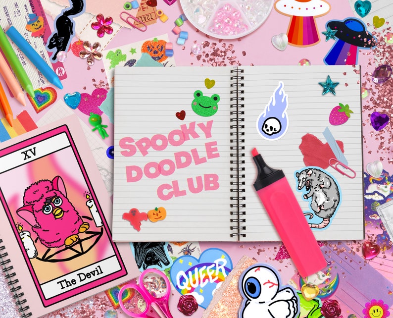 May include: A pink notebook with the words "Spooky Doodle Club" written on it. The notebook is surrounded by various stickers, including a pink fuzzy creature, a green frog, a skull, a rat, and a rainbow UFO.