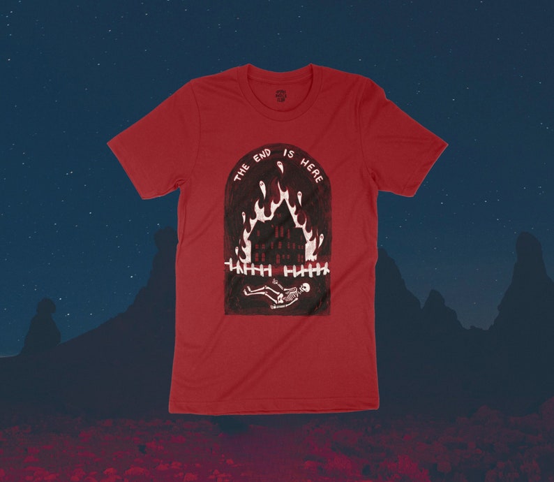 Op de afbeelding: Rood T-shirt met een afbeelding van een brandend huis en een skelet dat ervoor ligt. De tekst "The End Is Here" staat boven de afbeelding.