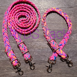 May include: A set of pink braided leather reins with colorful accents. The reins have gold metal buckles and clips.