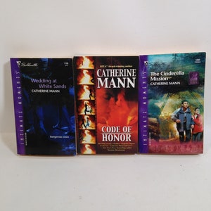 May include: Three paperback books with purple and white covers. The titles are "Wedding at White Sands", "Code of Honor", and "The Cinderella Mission". All three books are by Catherine Mann.
