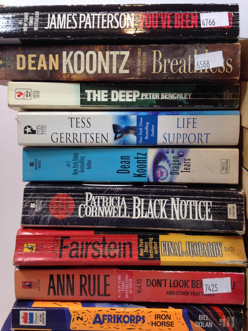 May include: A stack of hardcover books with various titles and authors, including James Patterson, Dean Koontz, and Patricia Cornwell. The books are in different colors, with visible text and labels.