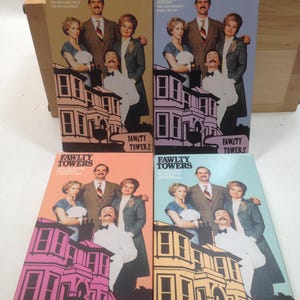 Puede incluir: Cuatro cintas VHS de la serie de comedia británica Fawlty Towers. Las cintas están dispuestas en una pila vertical. Cada cinta presenta un título de episodio diferente y una imagen colorida del hotel Fawlty Towers.