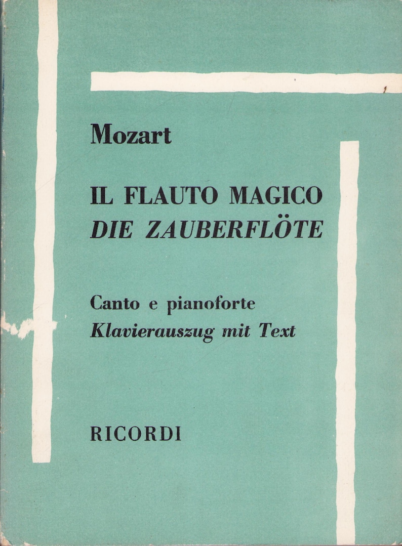 Puede incluir: Una partitura musical vintage con una cubierta turquesa y rayas blancas. La portada presenta el t&iacute;tulo "IL FLAUTO MAGICO DIE ZAUBERFL&Ouml;TE" de Mozart, con texto en italiano y alem&aacute;n. El nombre del editor, RICORDI, est&aacute; en la parte inferior.