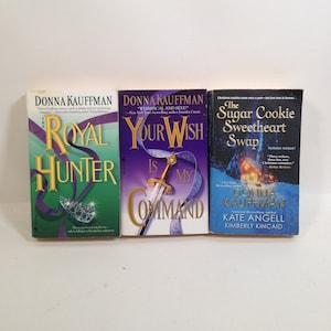 Könnte beinhalten: Drei Taschenbücher mit Romanen und bunten Umschlägen. Das erste Buch trägt den Titel "The Royal Hunter" und hat einen grünen Umschlag mit einer Krone und einem Schwert. Das zweite Buch trägt den Titel "Your Wish Is My Command" und hat einen violetten Umschlag mit einem Schwert und einer Krone. Das dritte Buch trägt den Titel "The Sugar Cookie Sweetheart Swap" und hat einen blauen Umschlag mit einer Winterszene und einem Keks.