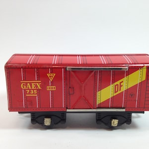 May include: A red toy train car with black wheels. The car has the text "GAEX 735" in yellow and a yellow diagonal stripe with "DF" on the side. White vertical stripes and a triangle symbol are also visible.