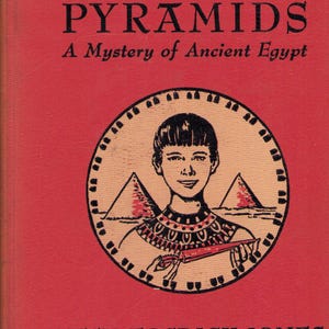 May include: A vintage book cover for "Boy of the Pyramids" by Ruth Fosdick Jones. The cover is red with black text and a circular illustration of a boy, pyramids, and hieroglyphic designs. The book is a mystery set in ancient Egypt.
