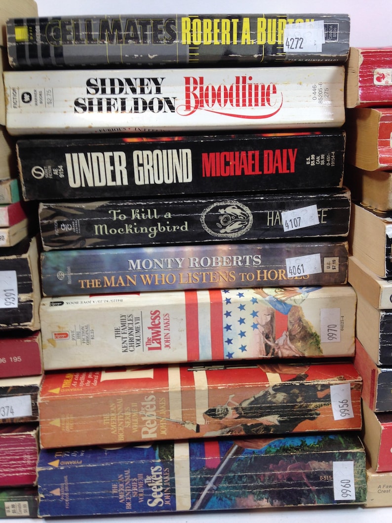 May include: A stack of vintage paperback books with titles including "Cellmates," "Bloodline," "Under Ground," and "To Kill a Mockingbird." The books have worn covers in various colors, with visible titles and author names.