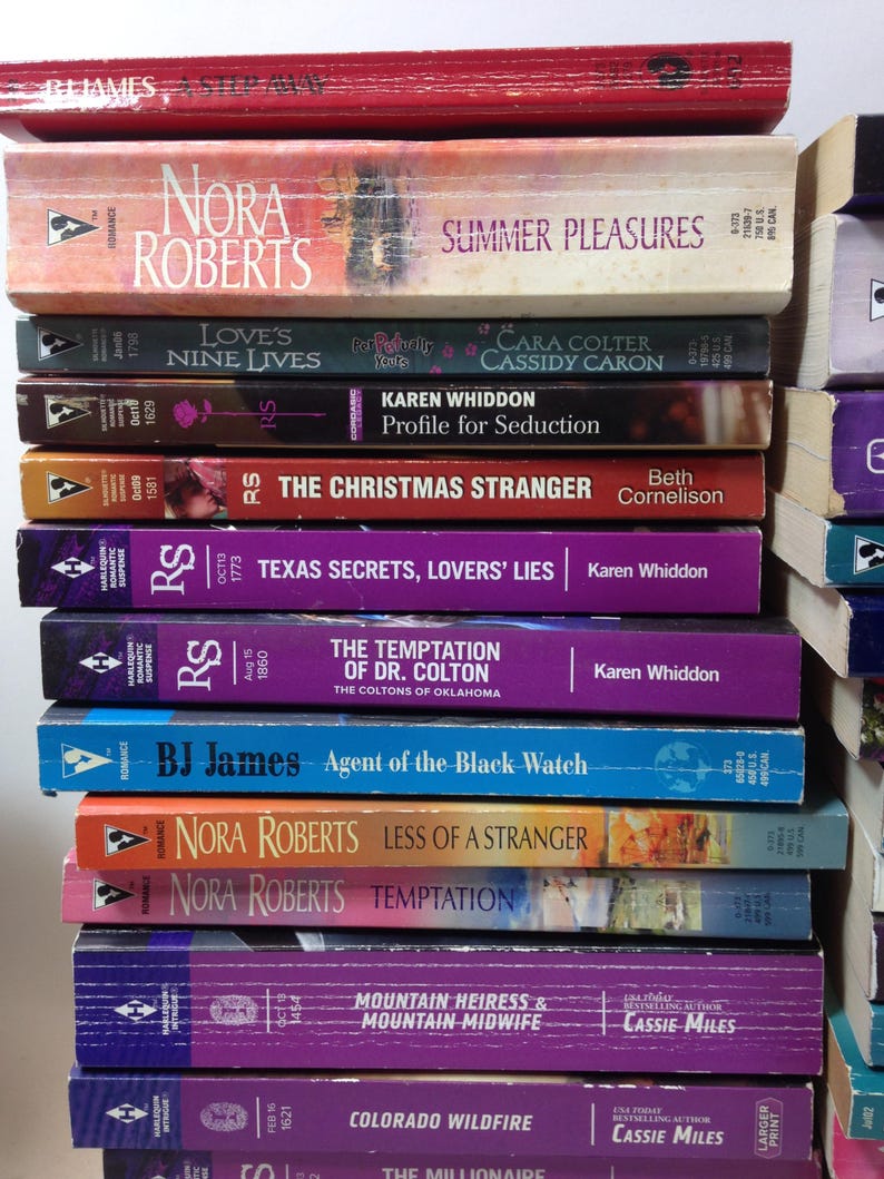 Może przedstawiać: Stos książek w miękkiej oprawie o tematyce romansu. Widoczne tytuły to "Summer Pleasures", "Love's Nine Lives" i "The Christmas Stranger". Książki ułożone pionowo, prezentują r&oacute;żnorodność autor&oacute;w i wzor&oacute;w okładek.