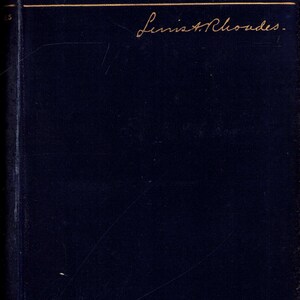 May include: A dark blue book cover with the title "MARIA STUART" in gold lettering. Below the title is a gold horizontal line, and beneath that is a handwritten signature. The book has a textured appearance.