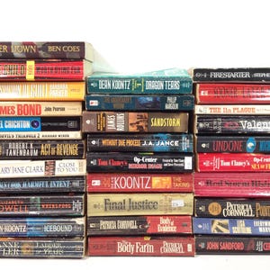 May include: A stack of hardcover books with various titles and authors. The spines display titles like "Power Down," "Firestarter," "James Bond," and "Sandstorm." The books are in various colors, including red, blue, and yellow.