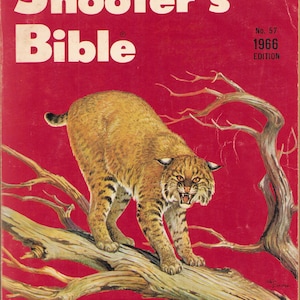 May include: The 1966 edition of the Shooter's Bible, No. 57, features a red cover with a bobcat standing on a tree branch. The text reads Shooter's Bible, No. 57, 1966 Edition, and The complete guide to firearms and accessories.