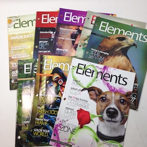 Op de afbeelding: Een verzameling "Elements" tijdschriften met diverse covers. Eén cover toont een hond met een roos, een andere een havik, en andere tonen tekst en afbeeldingen. De tijdschriften liggen op een witte ondergrond.
