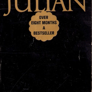 May include: A vintage paperback book cover for "Julian" by Gore Vidal. The title is in gold lettering, with the author's name above. A gold-colored sticker reads "Over Eight Months A Bestseller". The cover is black with white text.