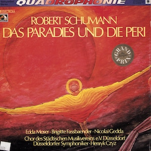Puede incluir: Una portada de álbum de vinilo vintage con el título "DAS PARADIES UND DIE PERI" de Robert Schumann. La portada presenta un diseño abstracto rojo y naranja con una figura dorada. El álbum es una grabación estéreo cuadrofónica.
