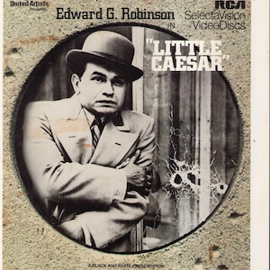 May include: A black and white RCA SelectaVision VideoDisc cover for the film Little Caesar starring Edward G. Robinson. The cover features a circular portrait of a man in a suit and bowler hat, with the text United Artists Presents, Little Caesar, and A Black and White Presentation.