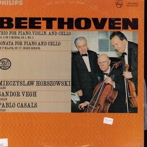 May include: A vintage vinyl record cover featuring an orange background with black text reading BEETHOVEN, TRIO FOR PIANO, VIOLIN, AND CELLO, and SONATA FOR PIANO AND CELLO. A photograph shows three men in formal black suits and bow ties.