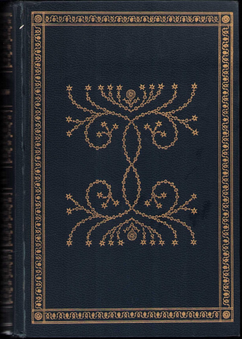 Pu&ograve; includere: Una copertina di libro blu scuro con un design decorativo dorato. La copertina presenta un motivo floreale dorato con stelle e un bordo decorativo. Il libro sembra essere un'edizione antica o vintage.