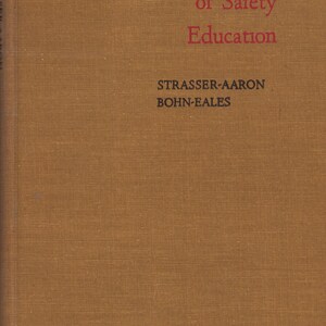 May include: A hardcover book with a textured, brown cover. The title "Fundamentals of Safety Education" is printed in red, with the author's names, Strasser-Aaron and Bohn-Eales, in black. The book's spine is visible on the left.