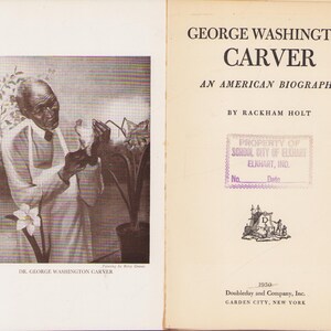 May include: An open book with a sepia-toned portrait of George Washington Carver on the left page. The right page displays the title "George Washington Carver: An American Biography" and a stamp from School City of Elkhart, Ind.