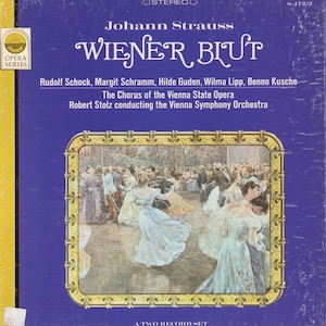 May include: Vintage vinyl record album cover for "Wiener Blut" by Johann Strauss. The cover is blue with gold lettering and a framed illustration of a ballroom scene. The Opera Series logo is in the upper left corner.