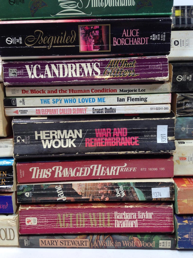 May include: A stack of vintage paperback books with titles like "Beguiled," "War and Remembrance," and "This Ravaged Heart." The books have colorful covers and varying sizes, showcasing a collection of classic literature.