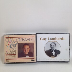 May include: Two compact disc cases featuring Guy Lombardo and his Royal Canadians. The left case has a photo of Guy Lombardo and the text "Guy Lombardo & His Royal Canadians Their Greatest Hits and Finest Performances". The right case has a photo of Guy Lombardo and the text "Guy Lombardo Essential Gold 3CDs Dearie Anniversary Song Enjoy Yourself Managua, Nicaragua Penny Serenade Bon Hoo Tum My Own Grandpa Easter Parade".