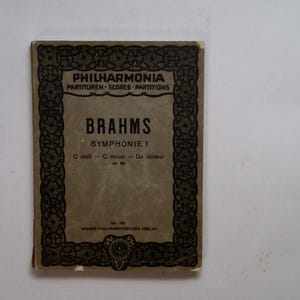 Op de afbeelding: Een vintage muziekpartituur voor Brahms' Symfonie nr. 1 in c-mineur. De omslag heeft een decoratieve rand met de titel "Philharmonia Partituren - Scores - Partitions" en de naam van de componist "Brahms" in vetgedrukt.