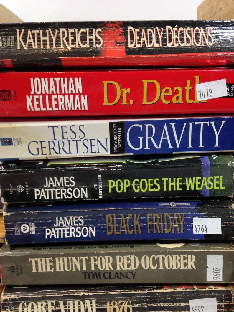 May include: A stack of hardcover books with titles including "Deadly Decisions," "Dr. Death," "Gravity," "Pop Goes the Weasel," "Black Friday," and "The Hunt for Red October." The books are in various colors, with visible author names.