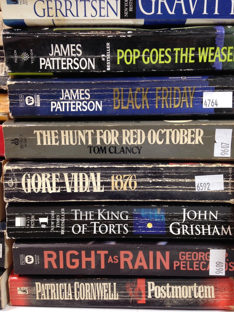 May include: A stack of hardcover books with various titles and authors visible. Titles include "Pop Goes the Weasel" by James Patterson, "Black Friday" by James Patterson, and "The Hunt for Red October" by Tom Clancy. The books are in various colors.
