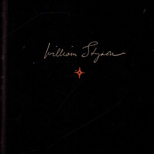 May include: A black book cover with the name "William Styron" in gold script. A small, red four-pointed star is centered below the name. The cover has a slightly textured appearance.
