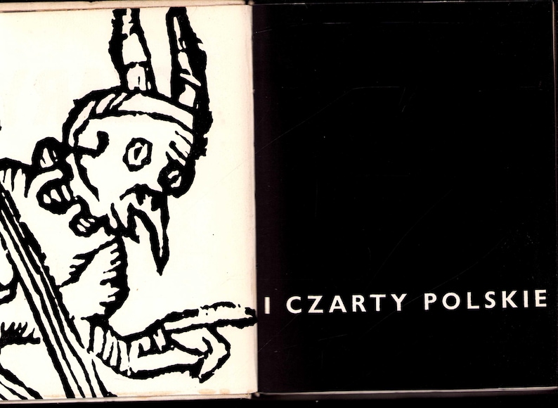 May include: Open book with a black and white illustration of a horned figure with a long beard and pointed finger. The text "I CZARTY POLSKIE" is printed in white on the right page. The book has a black background.